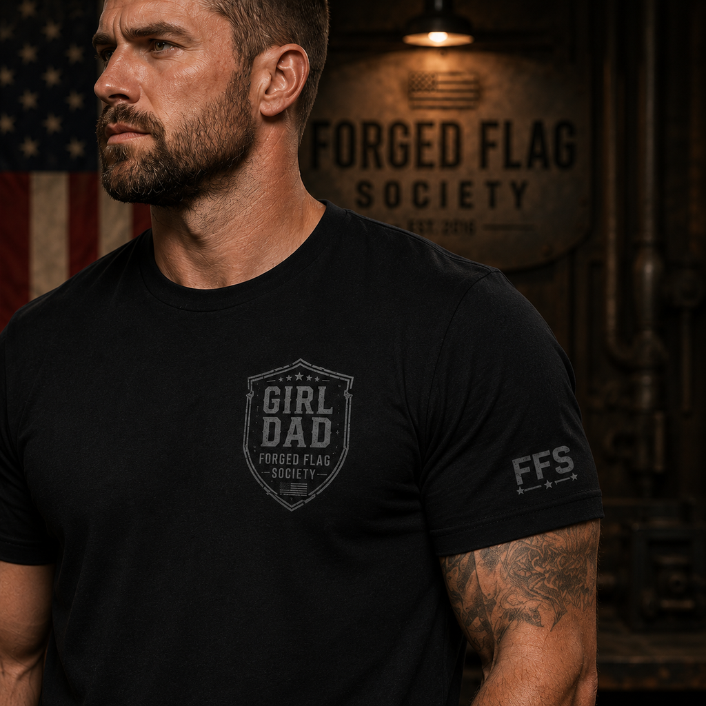 Man wearing a black t-shirt with 'Girl Dad' and 'Forged Flag Society' logos in a dimly lit room.